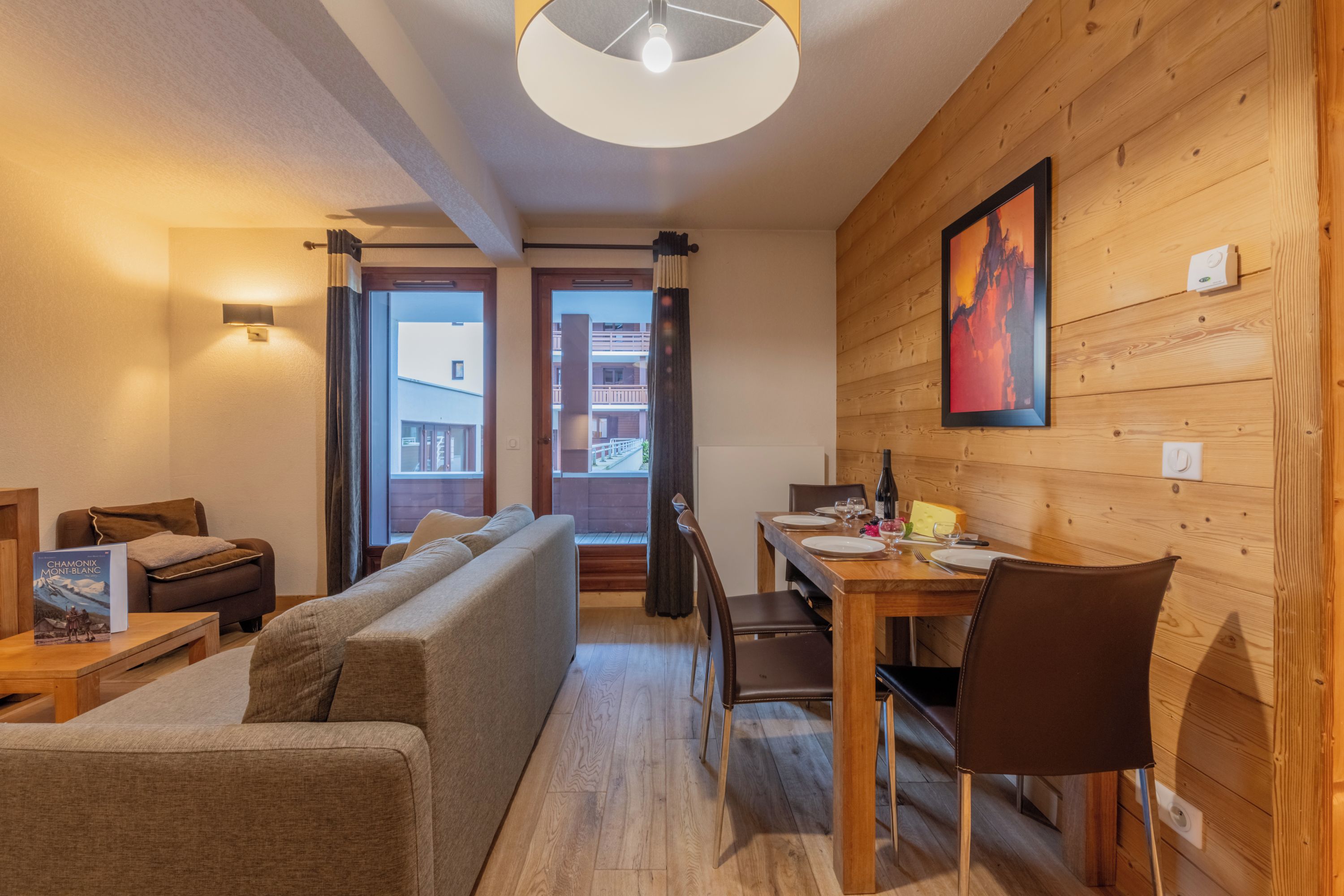 Una habitación acogedora con una pared de madera, una mesa de comedor con sillas, un sofá y una ventana con cortinas.