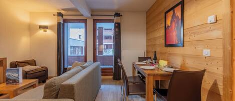 Una habitación acogedora con una pared de madera, una mesa de comedor con sillas, un sofá y una ventana con cortinas.