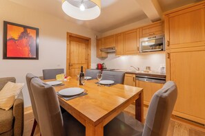 A modern kitchen with wooden cabinets, a dining table set for four, and a painting on the wall. - l Ours Bleu Apartments (Vallorcine)