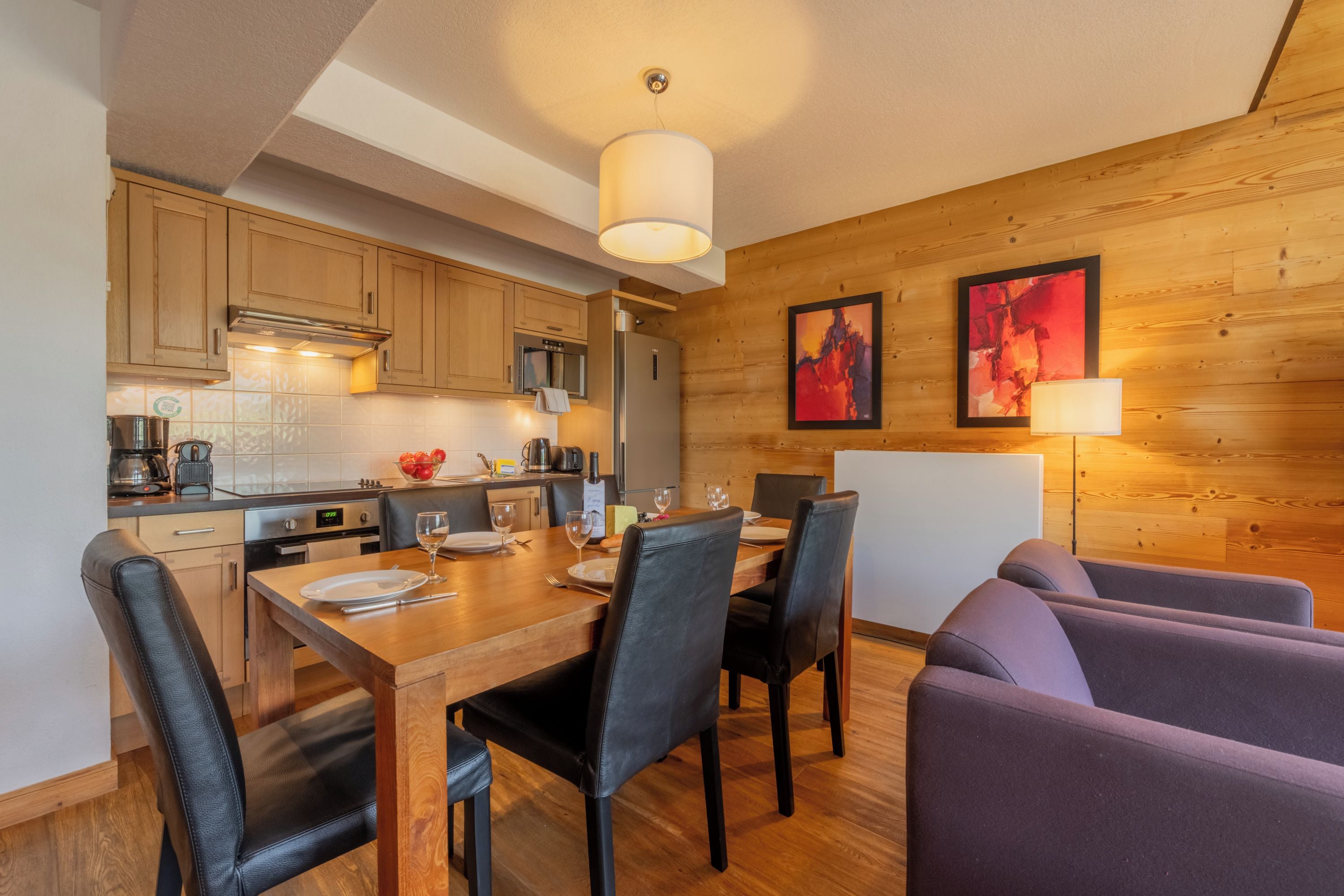 A modern kitchen with wooden cabinets, a dining table set for four, and a sofa in the dining area.