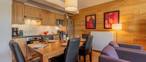 A modern kitchen with wooden cabinets, a dining table set for four, and a sofa in the dining area.