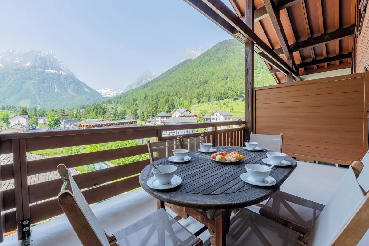 A wooden deck with a table set for dining, overlooking a mountainous landscape.