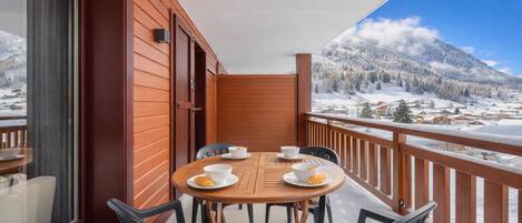 Un balcón con una mesa y sillas de madera, con vista a un paisaje montañoso nevado.