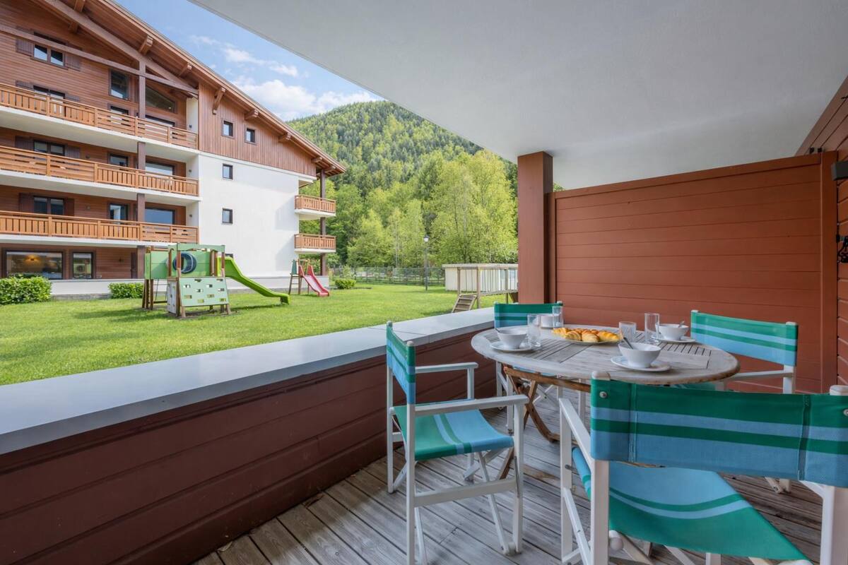 A balcony with a table and chairs, a playground, and a mountain view.