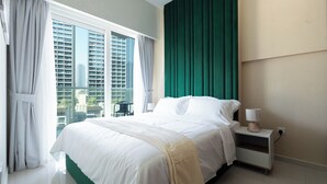 Une chambre d’hôtel avec un grand lit, une table de chevet, une lampe et une vue sur le paysage urbain, visible à travers de grandes fenêtres.