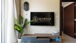 Un salon moderne avec un téléviseur à écran plat fixé au mur, une plante en pot, un meuble de rangement en bois et une porte sur le côté droit.