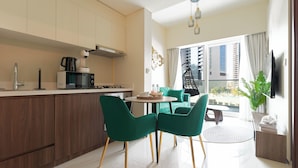 Une cuisine moderne équipée d’un four à micro-ondes, d’une machine à café et d’un fauteuil suspendu. On y trouve également un coin repas avec des chaises vertes et une table.