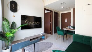 Un salon moderne doté d’un téléviseur à écran plat affichant le logo de « KEYROCK Holiday Homes », d’un coin repas avec des chaises vertes, d’une table basse et d’un canapé vert.