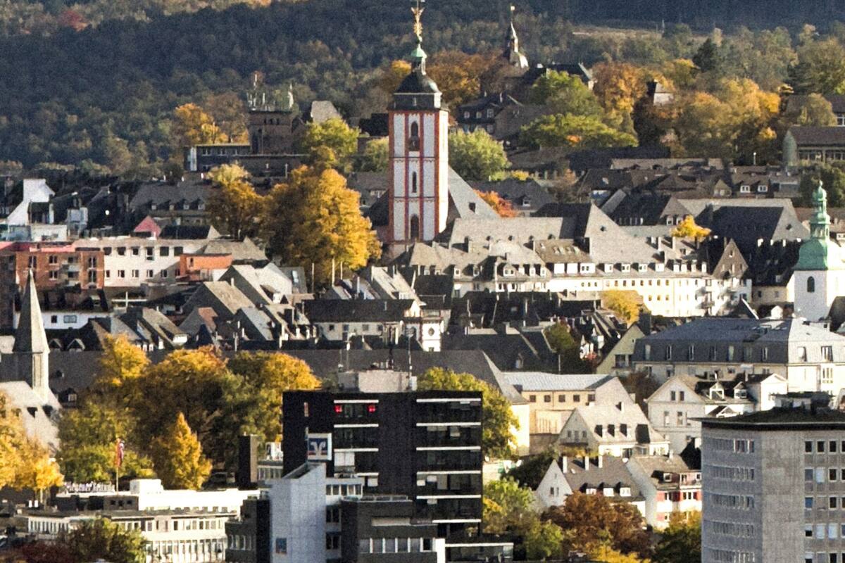 A town with a prominent tower, surrounded by residential and commercial buildings, and a hilly landscape in the background.