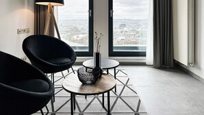 Een moderne woonkamer met een groot raam, twee zwarte stoelen, een kleine ronde tafel en een vloerlamp.