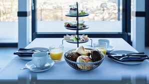 Een ontbijtsetting met een etagère vol desserts, een broodkom en een kop koffie op een tafel bij een raam.