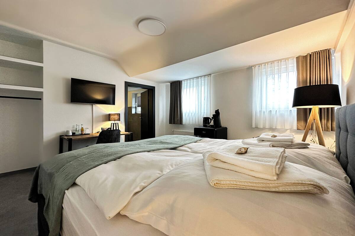 A hotel room with a large bed, a desk, a chair, a TV, a lamp, and a window with curtains.