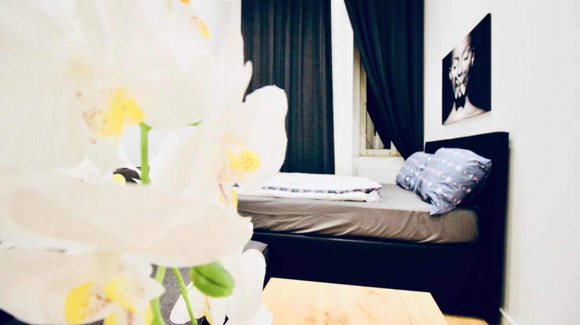 Ein Schlafzimmer mit einem Bett, einem Fenster mit Vorhängen und einem Wandbild.