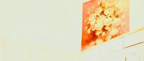 A bathroom with a white toilet, a wall-mounted paper towel dispenser, and a floral artwork above the toilet.