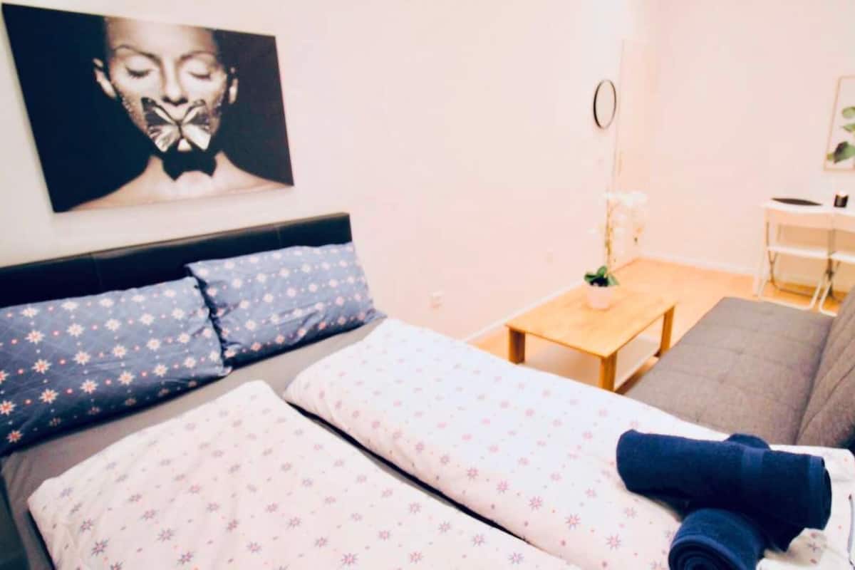 A neatly arranged bedroom with a bed, a sofa, a small table, and a desk.