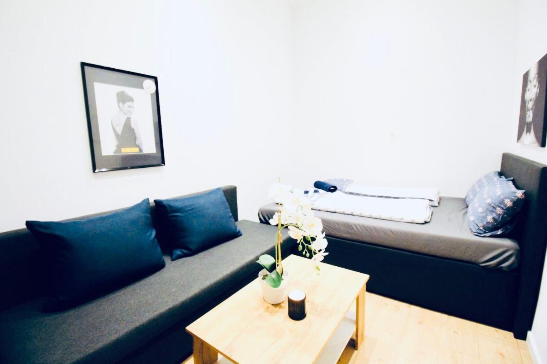 Ein modernes Wohnzimmer mit einem grauen Sofa, einem kleinen Holztisch und einem Bett mit grauem Matratze und blauen Kissen.