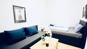 Ein modernes Wohnzimmer mit einem grauen Sofa, einem kleinen Holztisch und einem Bett mit grauem Matratze und blauen Kissen.