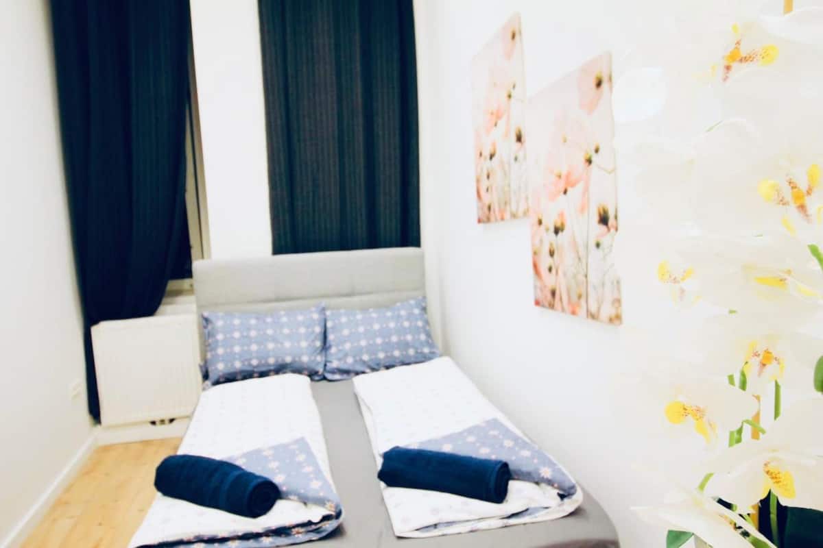 A hotel room with a bed, two pillows, a rolled-up towel, and a wall with floral artwork.