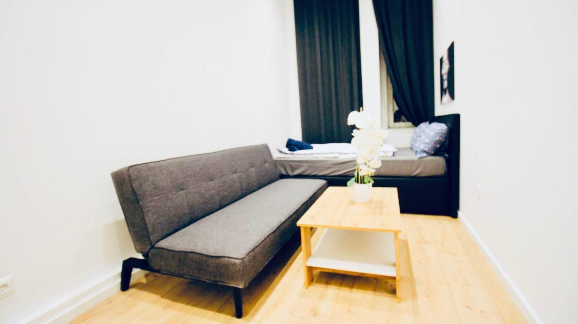 Ein modernes Wohnzimmer mit einem grauen Sofa, einem Holztisch und einem Bett mit grauem Kopfteil.
