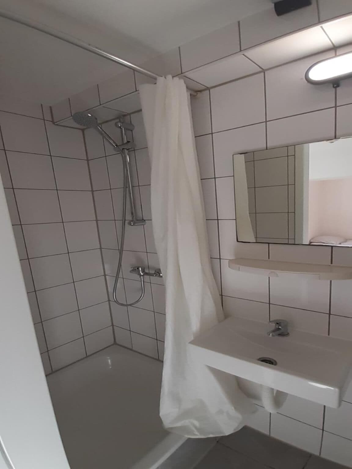 Un baño con ducha, lavamanos y espejo.