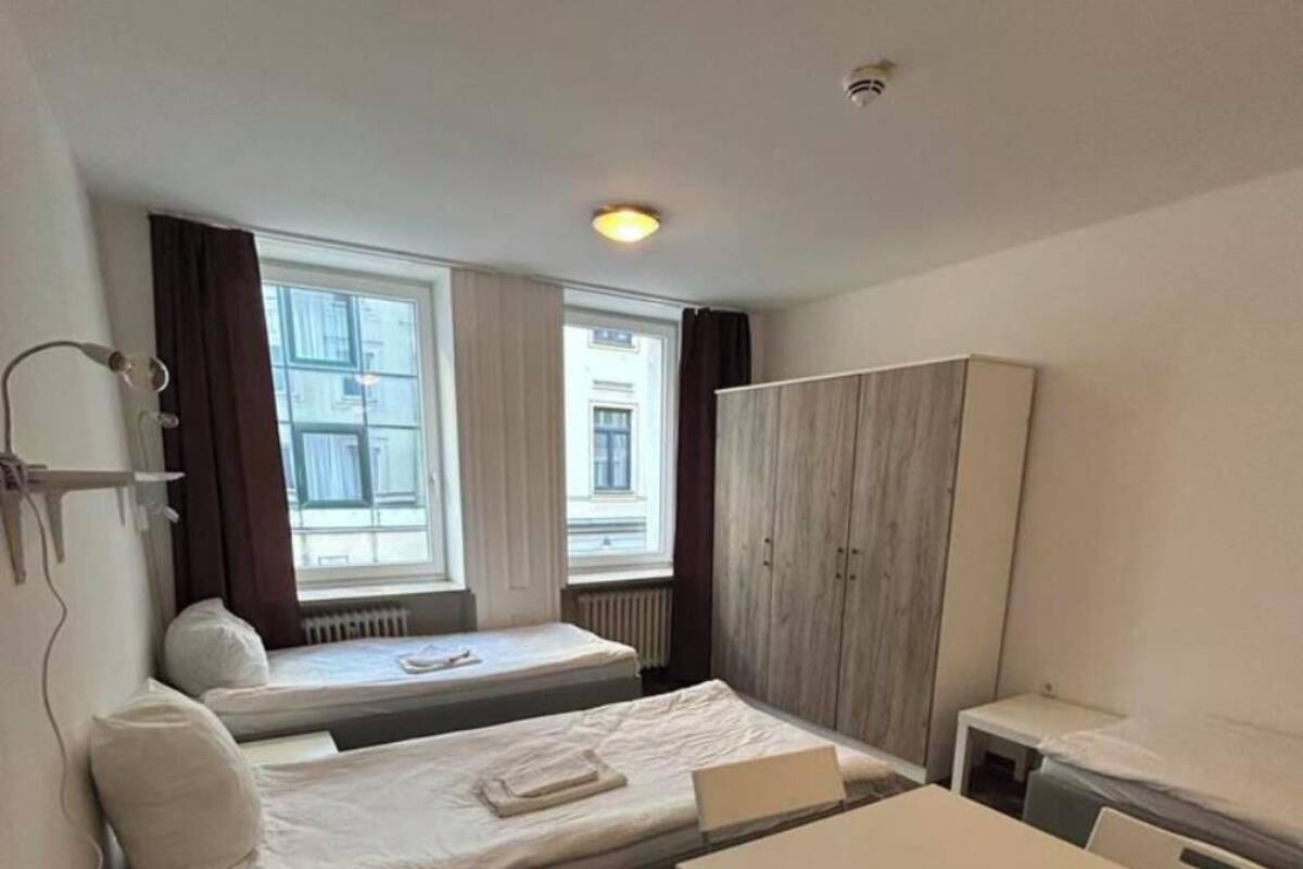 Une chambre d’hôtel de taille modeste, comprenant un lit, une petite table, une chaise, une armoire et une fenêtre avec des rideaux.