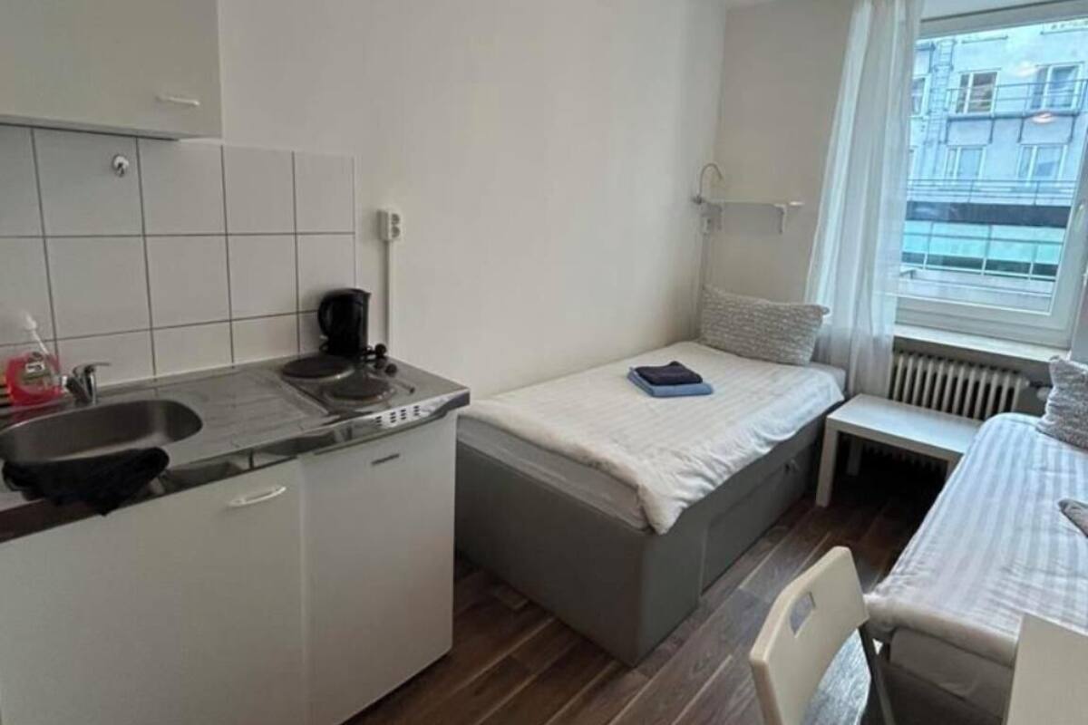 Une chambre d’hôtel compacte comprenant un coin cuisine, un lit, une petite table et une fenêtre donnant sur la ville.