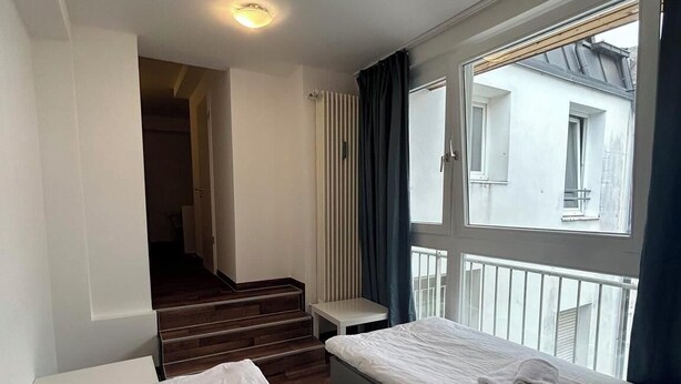 Ett hotellrum med två sängar, ett fönster med gardiner, ett element och en trappa som leder till ett annat rum.