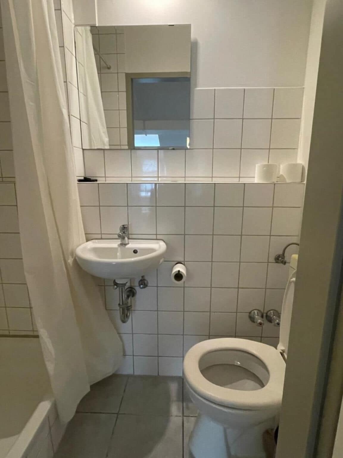 Un baño pequeño y funcional con un lavabo blanco, inodoro y un espejo sobre el lavabo.