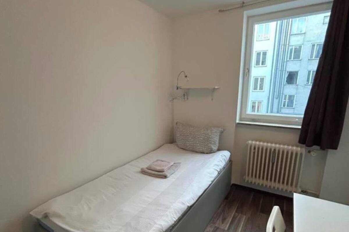 Une petite chambre avec un lit simple, une fenêtre, un radiateur et un bureau.