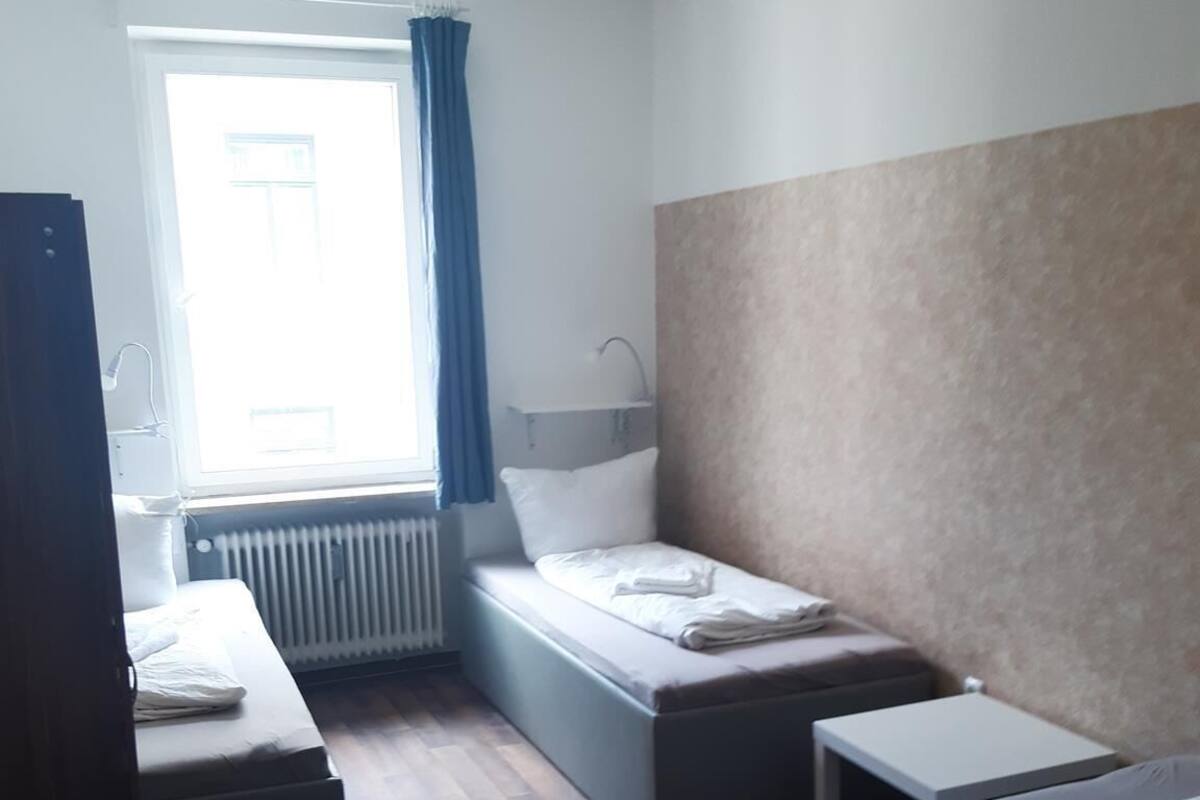 Une petite pièce bien éclairée, avec un lit simple, un bureau et une chaise.