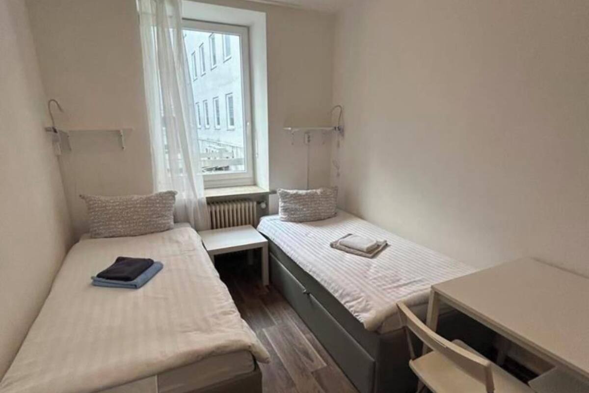 Une chambre d’hôtel de taille réduite, équipée de deux lits simples, d’un petit bureau et d’une chaise.