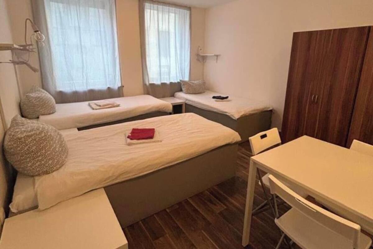 Une chambre de taille modeste, équipée de deux lits simples, d’une petite table, d’une chaise et d’une armoire.