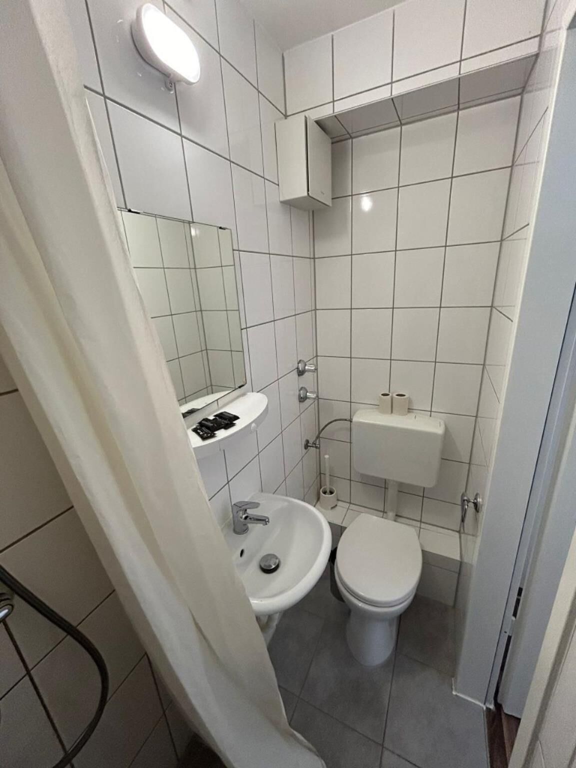 Un baño pequeño y limpio con lavamanos, inodoro y espejo blancos.