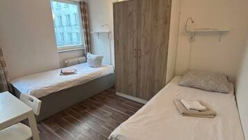 Ein kleiner, gut beleuchteter Raum mit zwei Betten, einem Schreibtisch und einem Fenster.
