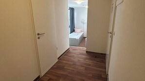 En smal hall med trägolv som leder till ett sovrum med en säng och ett fönster.