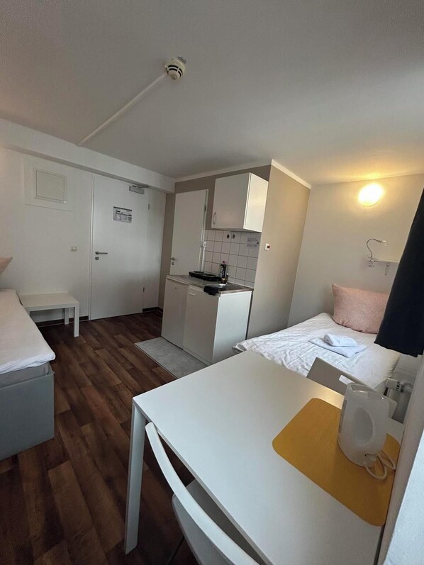 A compact hotel room with a kitchenette, a bed, a small table, and a chair. - 2-Rent Group Hostel Apartments SEN14 (Munich)