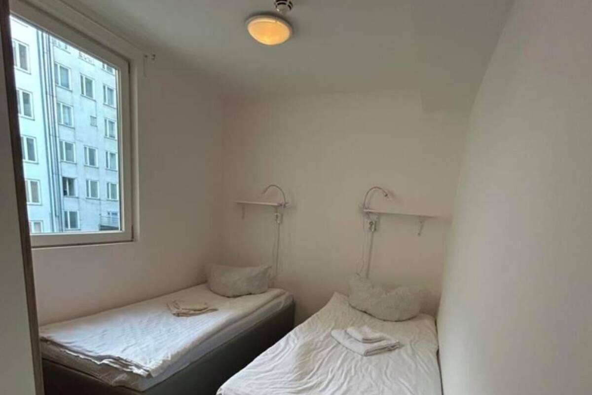 Une petite chambre, de taille modeste, comprenant deux lits simples, une petite table et une fenêtre donnant sur un bâtiment extérieur.