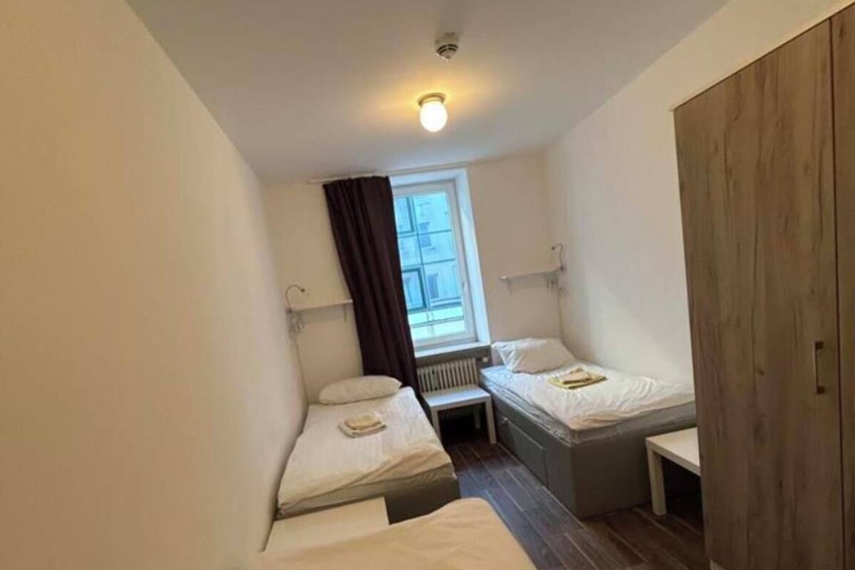 Une chambre d’hôtel de taille modeste, équipée de deux lits simples, d’une armoire en bois, d’une petite table et d’une fenêtre avec des rideaux.