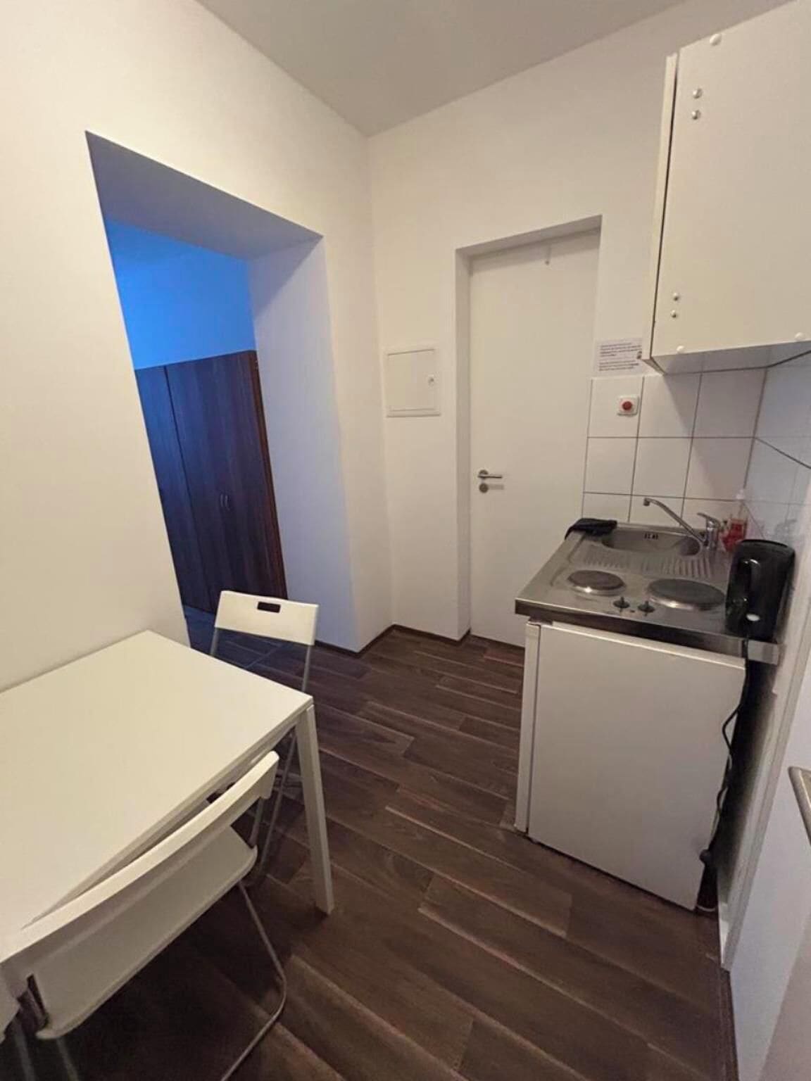 Cocina pequeña con una mesa y silla blancos, una encimera y una puerta con interruptor de luz.