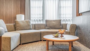 Una sala de estar moderna con un sofá seccional, una mesa de centro redonda de madera y un ventanal con cortinas.