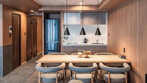 Una habitación de hotel moderna con piso de madera, una amplia mesa de comedor de madera con seis sillas, un refrigerador, un microondas y un horno empotrado.