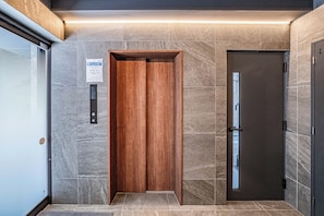An elevator with a wooden interior and a metallic door, set in a hallway with grey stone walls and a tiled floor.
