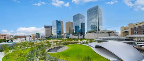 A modern urban landscape with high-rise buildings, a central green park, and a distinctive curved architectural feature.