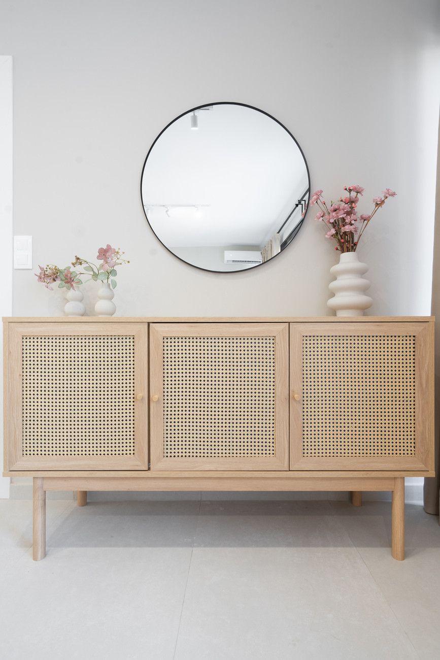 A wooden cabinet with a round mirror above it, flanked by two white vases with flowers.
