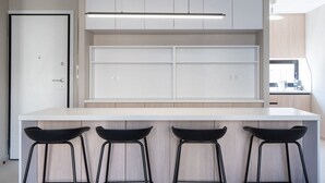 A modern kitchen with white cabinetry, a white countertop, and three black bar stools. - LIV - Deluxe 2BD Apartment in Athens (Athens)