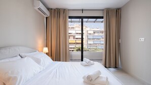 A hotel room with a bed, two pillows, a lamp, and a window with curtains. - LIV - Deluxe 2BD Apartment in Athens (Athens)