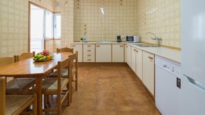 Een keuken met een eettafel, stoelen, een koelkast, een magnetron en een spoelbak.