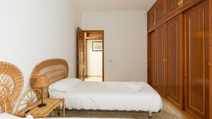 Een slaapkamer met twee eenpersoonsbedden, een houten garderobe en rieten meubels.