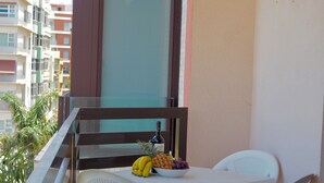 Een balkon met een tafel, stoelen en een schaal fruit.