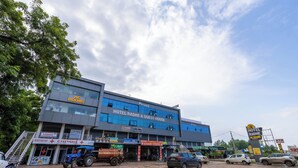 Een hotel genaamd "HOTEL RADHE & GUEST HOUSE" met een modern architectonisch ontwerp, met een opvallende ingang en diverse winkels op de begane grond.